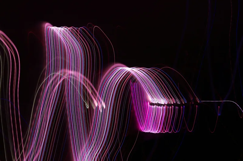 Long-exposure light streaks in pink and violet curving against a black background