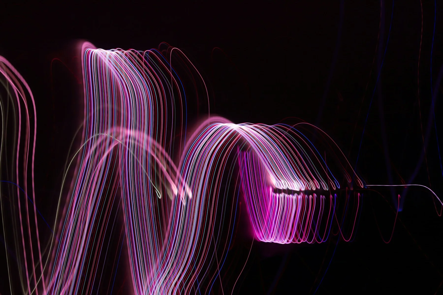 Long-exposure light streaks in pink and violet curving against a black background